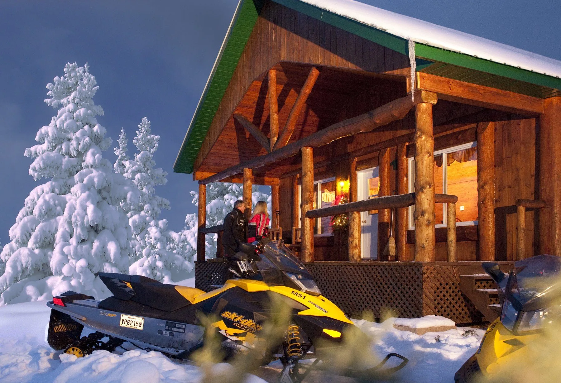 Chalet de troncos iluminado al crepúsculo, árboles escarchados y motonieves